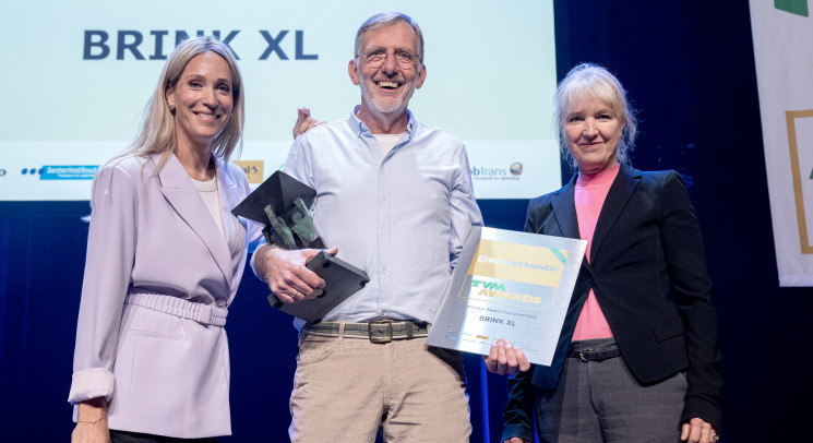 Twee vrouwen en een man staan lachend op een podium bij de uitreiking van de TVM Award Duurzaamheid aan Brink XL.